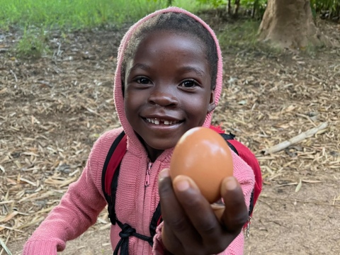 Zambian child in pink jacket holding up an egg.